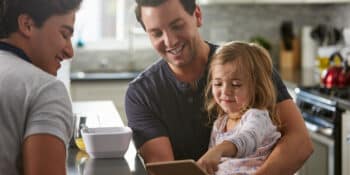 Two men looking after a young girl, sitting together in their kitchen.