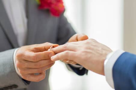 Where can you get married? A man placing a wedding ring on a man's finger.